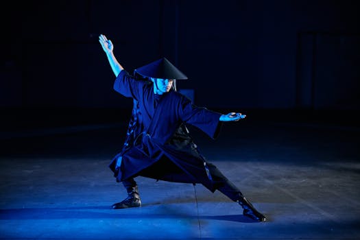 A martial artist dressed in traditional attire strikes a dynamic pose in an atmospheric indoor setting.